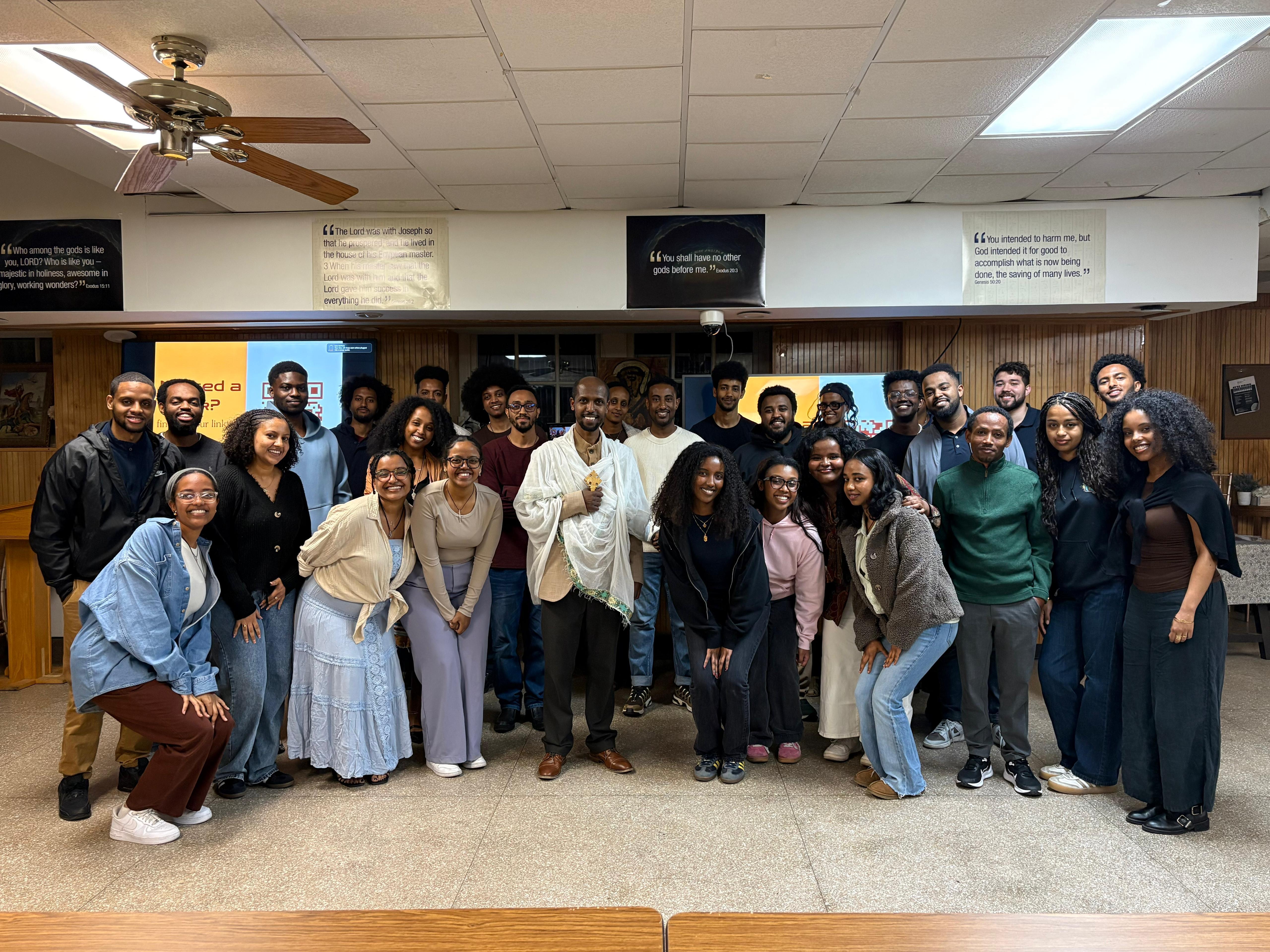 Kesis Tewodros poses with a large group of OTY NYC members in the parish hall